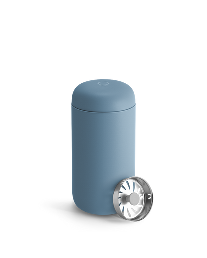 A Fellow Carter Move Mug in blue with a silver strainer lid leaning against it.